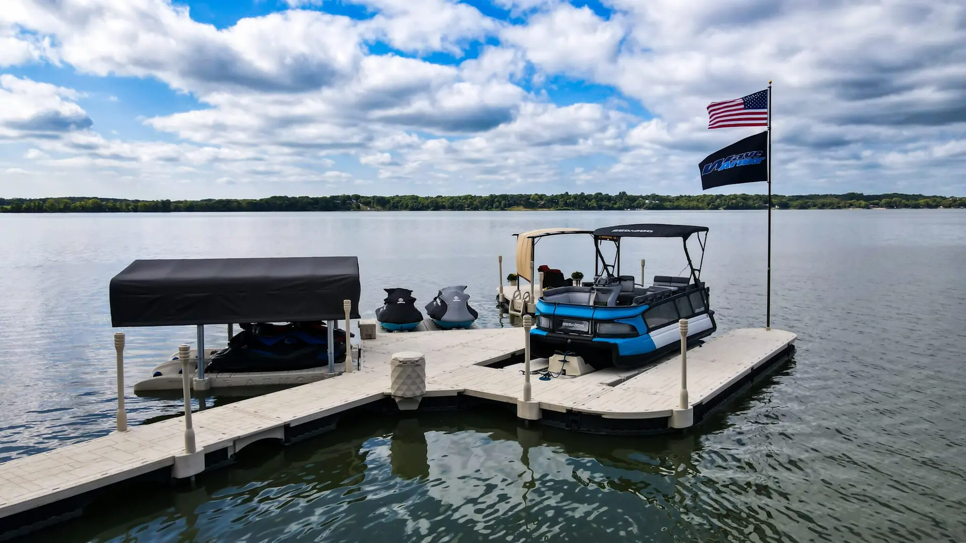Wave Armor floating dock system with a pontoon boat, PWC ports, and American flag on a calm lake.