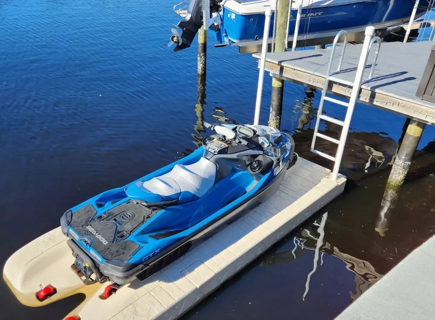 Best Jet Ski Docks: A blue and black Sea-Doo GTX personal watercraft parked on a tan floating dock next to a wooden pier with a swim ladder.