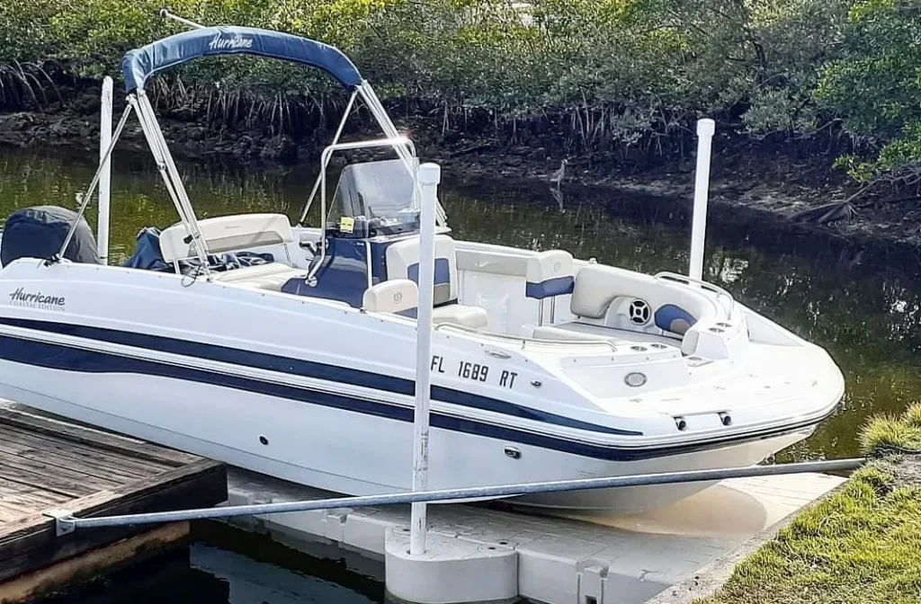 Durability of Wave Armor:A white and blue Hurricane Coastal Edition deck boat secured to a tan floating drive-on boat lift in a shallow waterway.