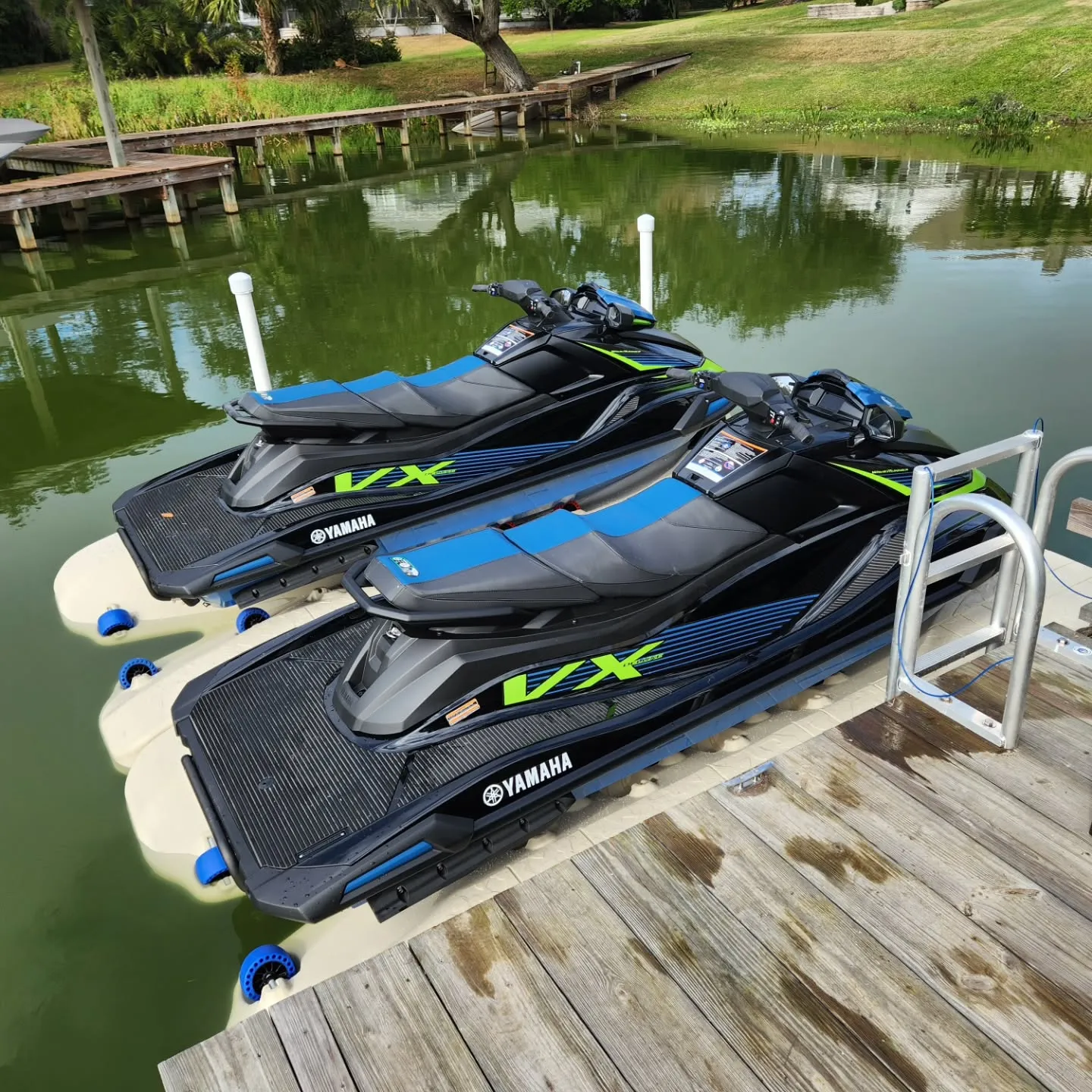Jet Ski Docks:Two black Yamaha VX WaveRunners with neon green accents docked on tan floating PWC ports with blue rollers, attached to a wooden residential dock.
