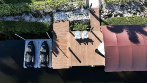 Top-down view of a dock with a covered boat lift and jet ski lifts on a Florida waterfront property.