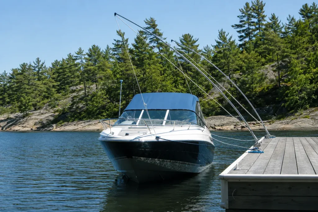 Mooring whips securing a cabin boat away from a wooden dock on a calm lake surrounded by rocks and pine trees.